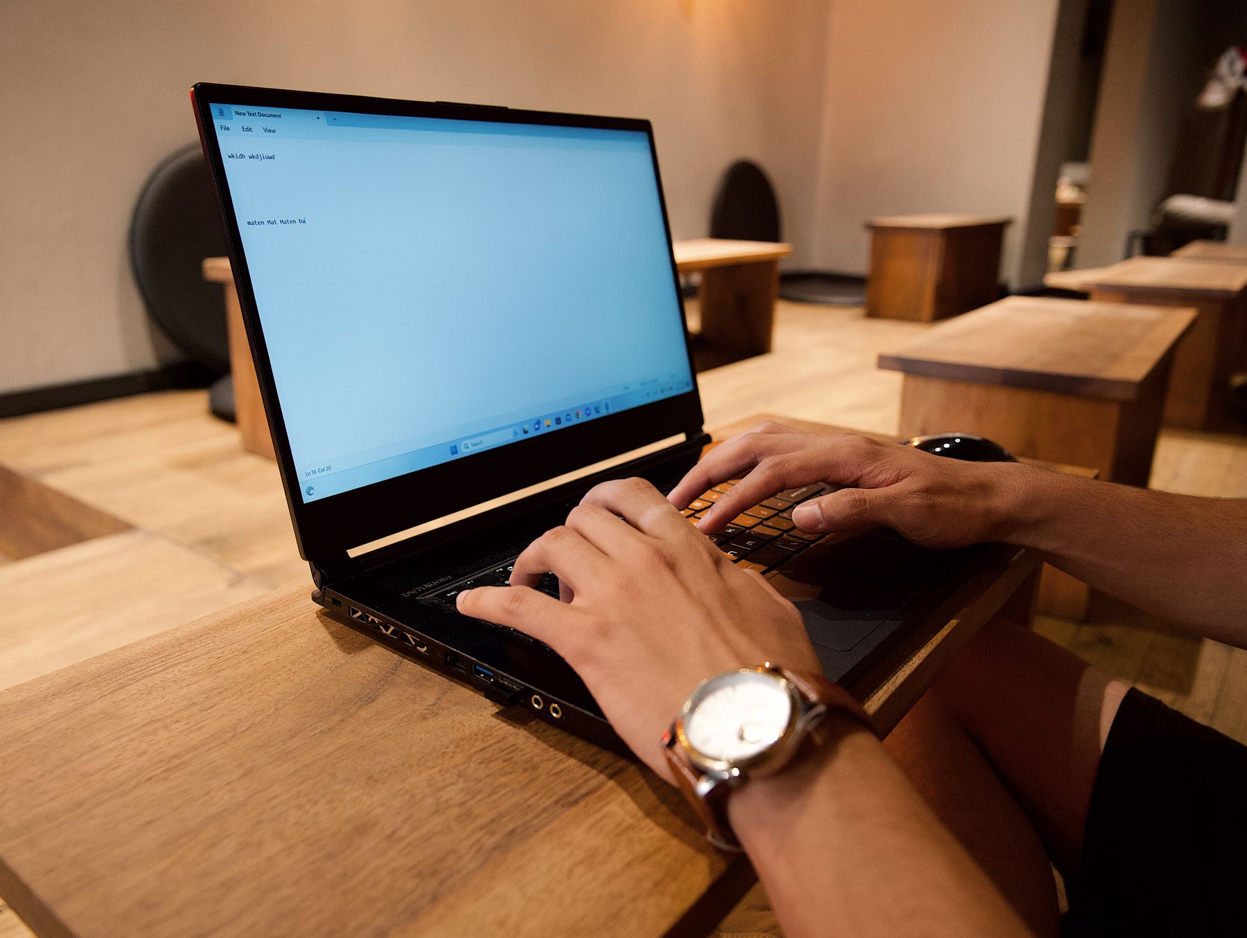 Hands type a document on a laptop at a wooden workspace.