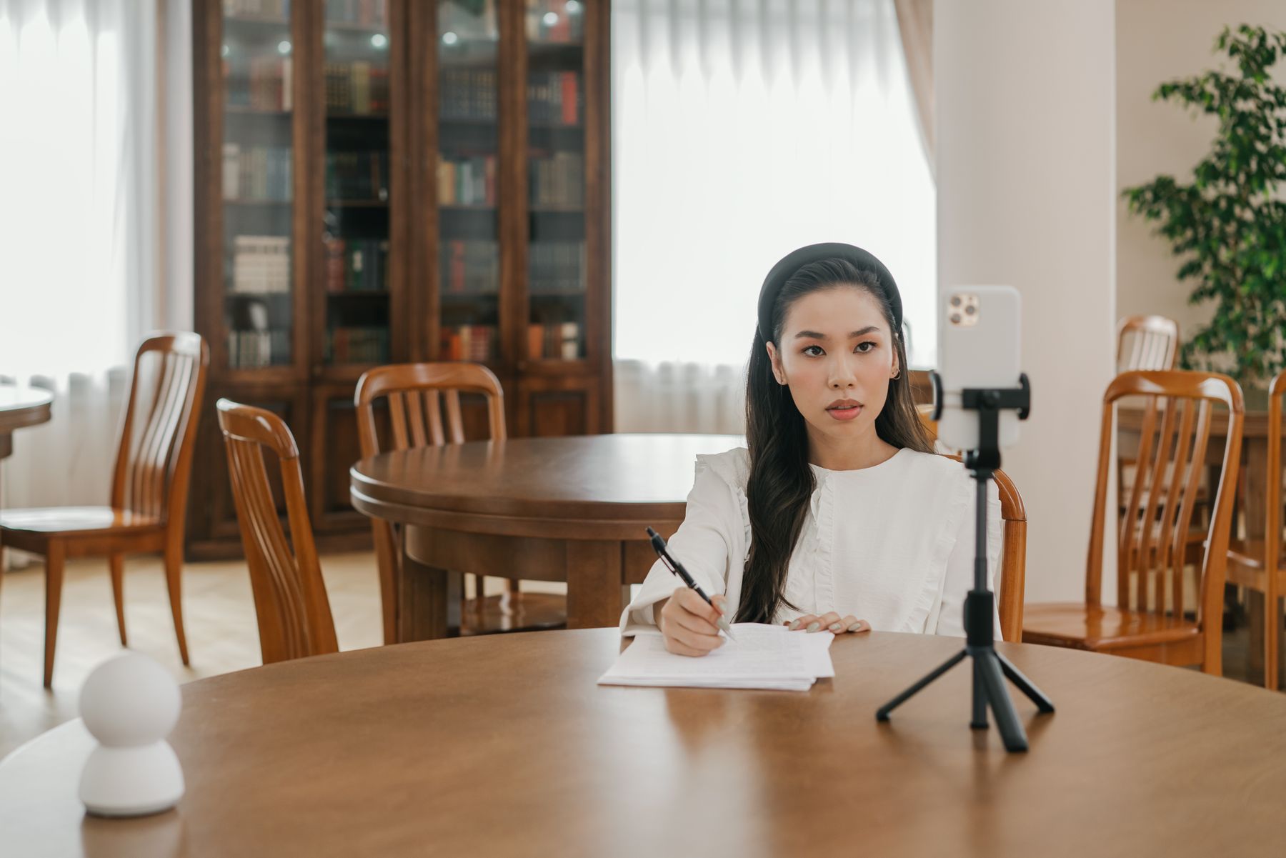 An adult creator records a lesson with a smartphone, notebook and pen.