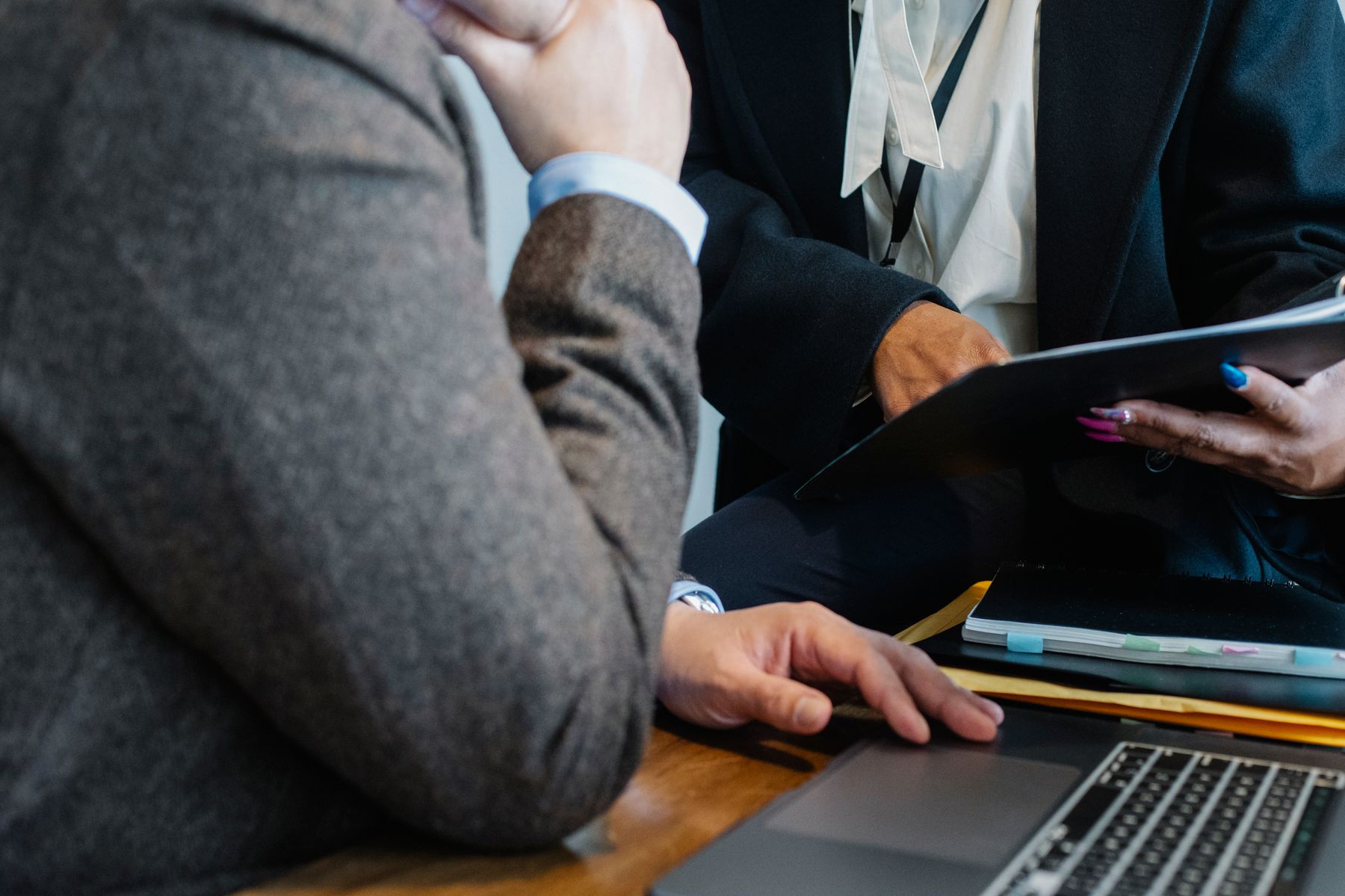 Two professionals review a folder of documents beside a laptop and tabbed notebook.