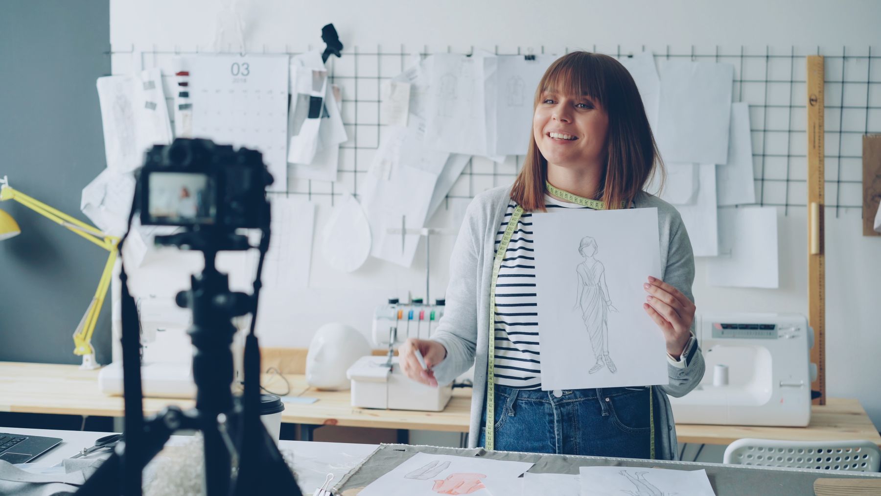 An independent designer presents a sketchbook while recording a tutorial in her studio.