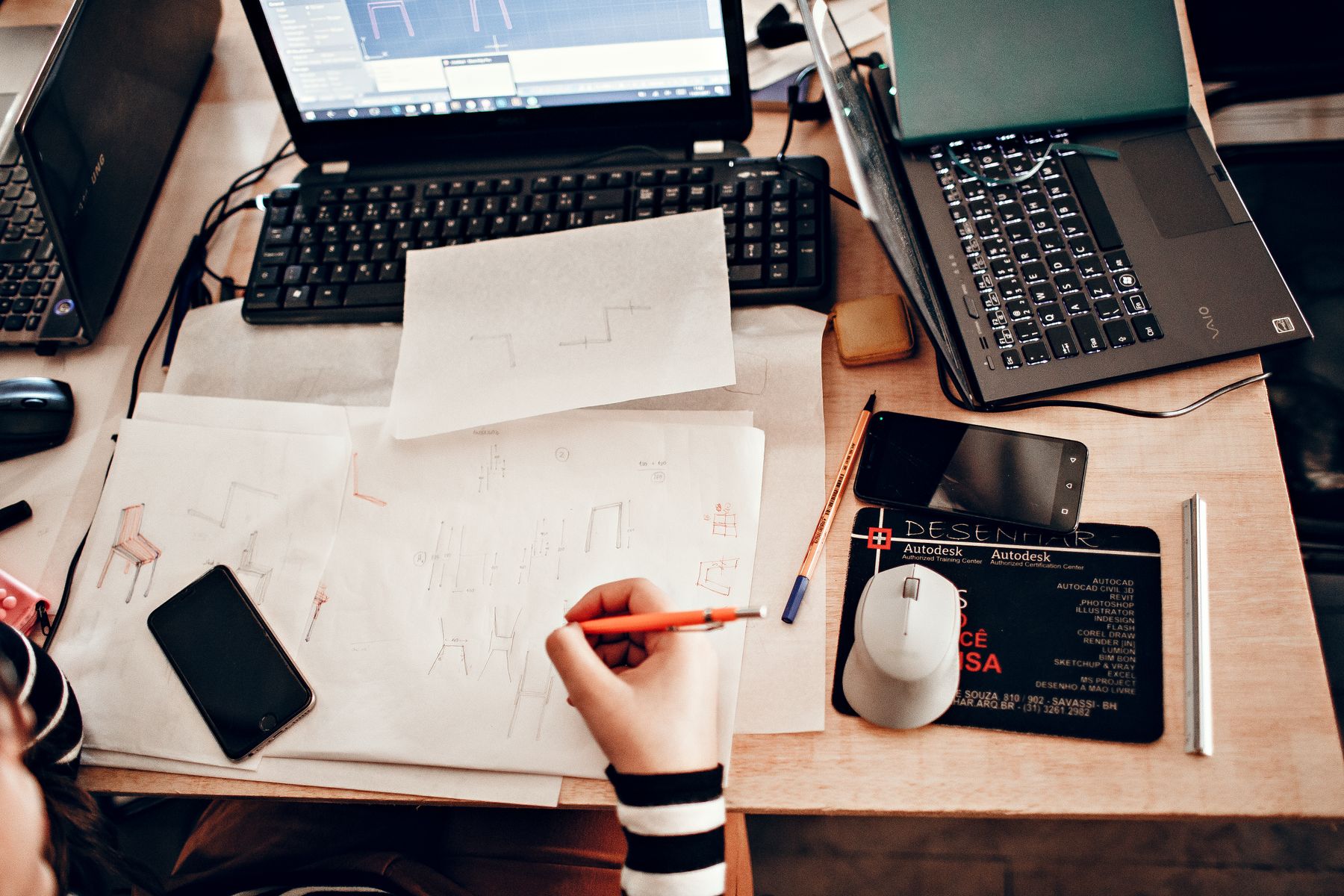 An overhead view of a creator sketching in a workbook beside a laptop and drawing tools.