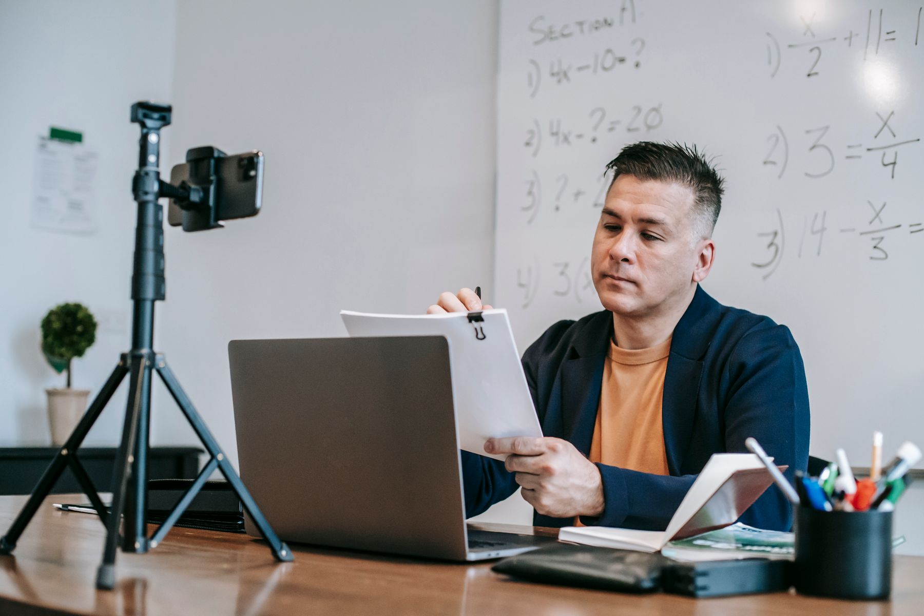 An educator reviews lesson papers beside a laptop and a recording setup.