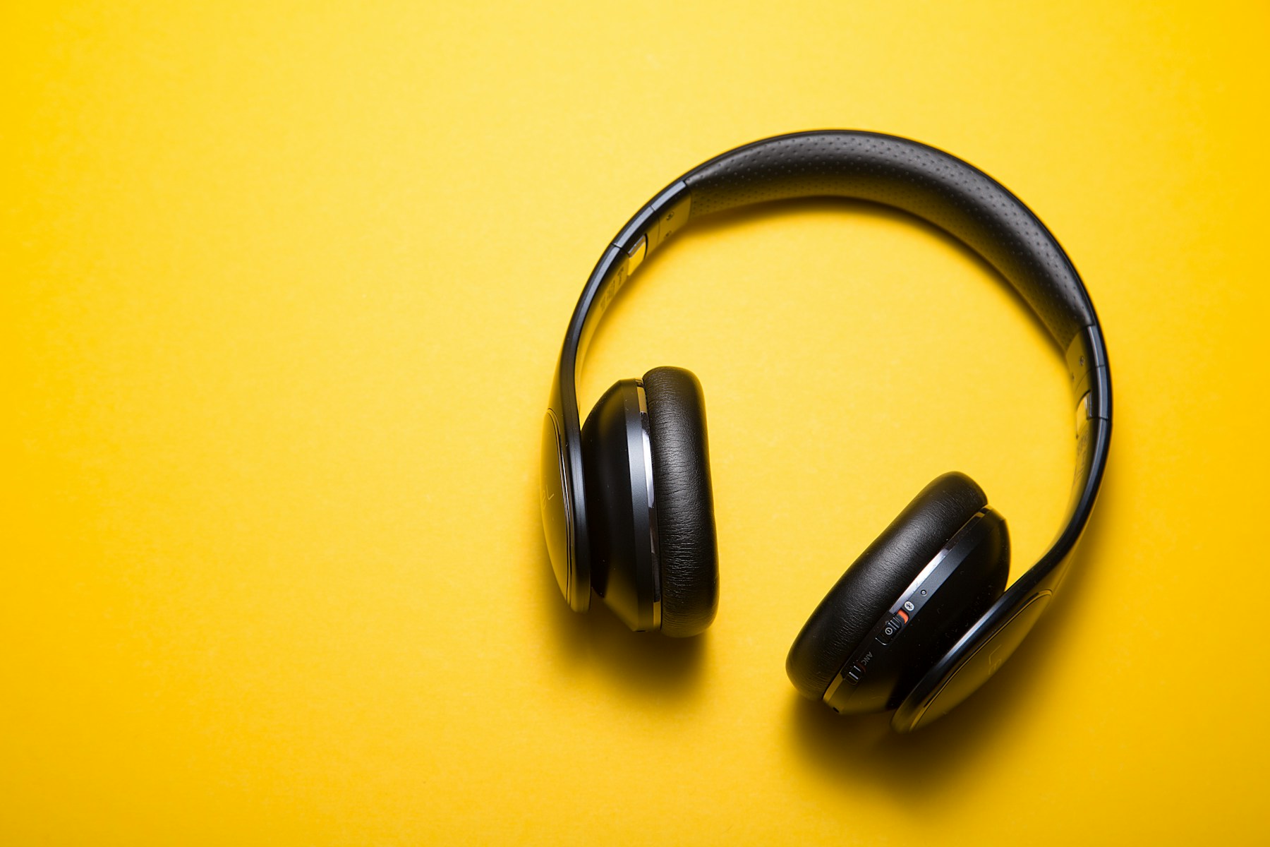 Black wireless headphones on a vivid yellow studio background
